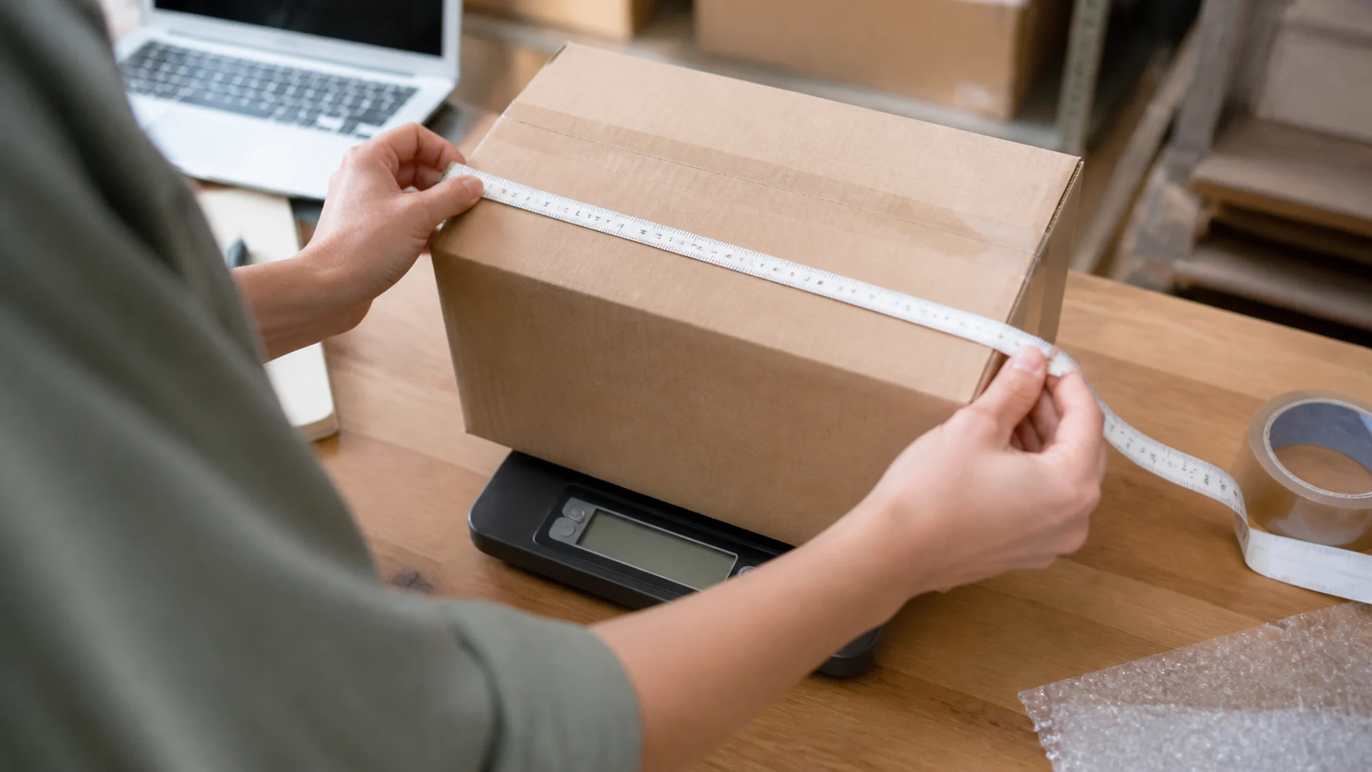 Online seller measuring a cardboard parcel while it rests on a digital scale.